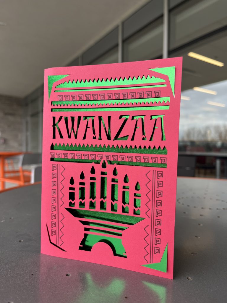 Red and green card featuring a kinara and candles, and the word Kwanza