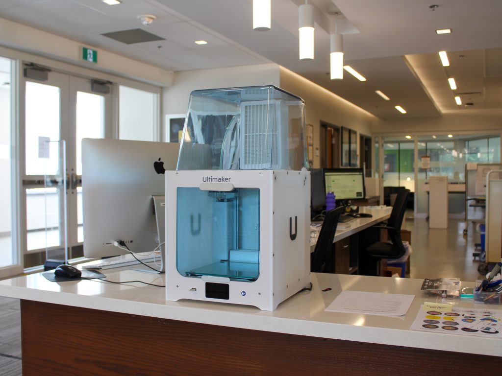 A white Ultimaker 3D printer with a blue window sits on the FGL service desk.